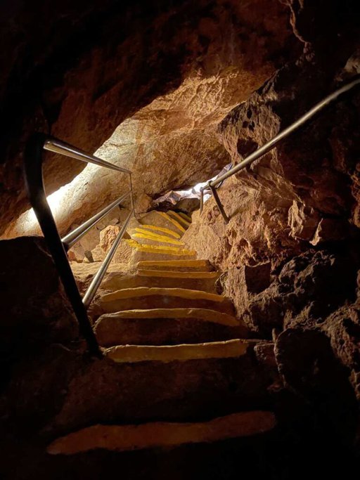 A narrow, illuminated staircase inside Ngilgi Cave, surrounded by rocky walls. This image is relevant to a Ngilgi Cave review by illustrating the cave's unique and adventurous pathways