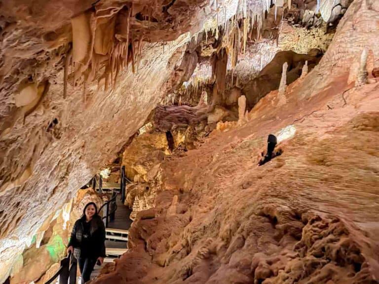 A woman walks along a well-lit pathway inside Ngilgi Cave, surrounded by intricate stalactite and stalagmite formations. This image shows the beautiful and accessible interior of the cave.