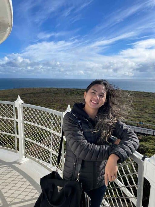 The author, Kate, standing on the platform on top of Cape Naturaliste Lighthouse, with a beautiful view of the coastline in the background. This photo relates to the Cape Naturaliste Lighthouse Guide by highlighting the stunning panoramic views visitors can enjoy from the lighthouse, making it a memorable spot for photography and enjoying the scenic beauty of the Indian Ocean and surrounding landscapes.