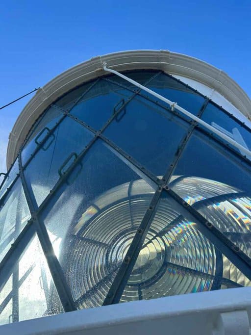 The image shows the top of the Cape Naturaliste Lighthouse, focusing on its large Fresnel lens. This photo relates to the "guide to Cape Naturaliste Lighthouse" post by showcasing the lighthouse's crucial feature, which aids in guiding ships safely along the coast. The lens' intricate design and historical significance are central to the lighthouse's story and its role in maritime navigation.