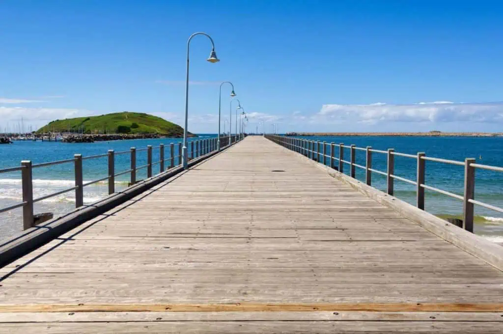 Long timber jetty stretching out into the ocean at Coffs Harbour with Muttonbird Island in the background, a peaceful photo spot along any Sydney to Byron Bay road trip itinerary.