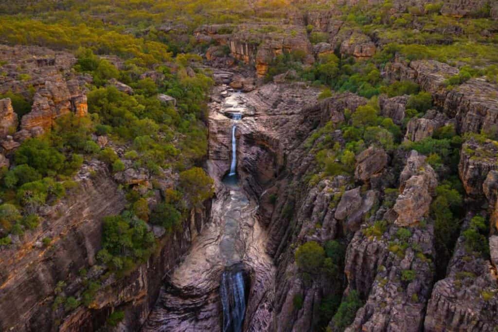 Jim Jim Falls in Kakadu National Park, Northern Territory, viewed from above, showcasing the waterfall's dramatic drop into a rocky gorge surrounded by dense greenery, highlighting the rugged beauty of waterfalls in Australia.