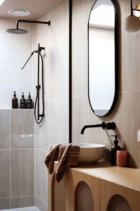 An elegantly designed bathroom within the best luxury cabin near Derby, featuring a sleek, black shower fixture, an oval mirror, and a minimalist vanity with organic bath products, reflecting the cabin's sophisticated amenities and serene bathroom experience.