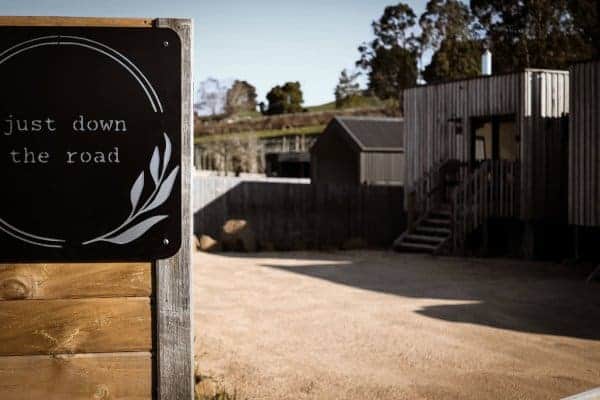 The welcoming signpost for a luxury cabin in Branxholm, reading 'just down the road', with a backdrop of the cabin's exterior and surrounding serene landscape, highlighting the cabin's secluded yet accessible location for a peaceful getaway.