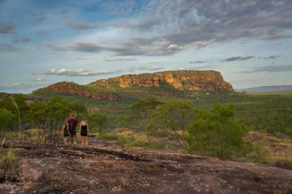 Hikers walking towards a scenic view of rocky cliffs at Kakadu National Park in the Northern Territory, Australia, during sunset. This image highlights one of the unmissable sunsets in Australia, featured in the blog post about top sunset locations.