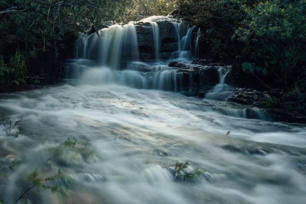 Kellys Falls in the Royal National Park, NSW, with water cascading over rocks surrounded by lush greenery, representing the tranquil beauty of Australia's waterfalls and their significance in natural exploration.