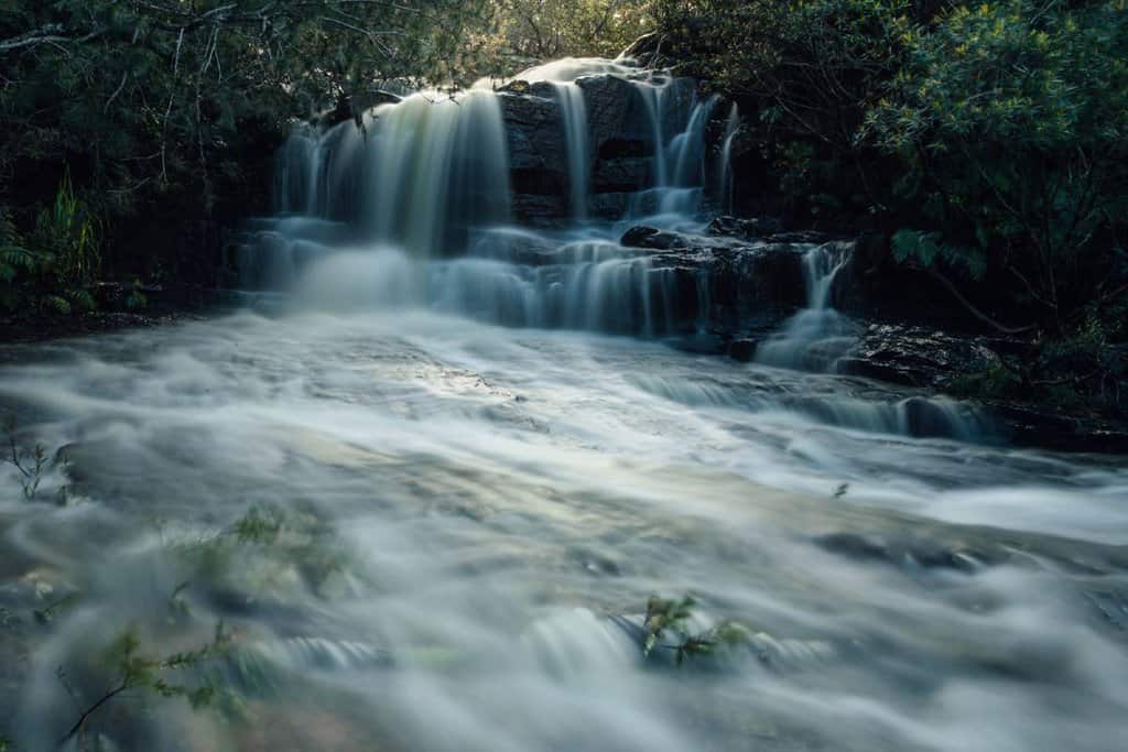 Kellys Falls in the Royal National Park, NSW, with water cascading over rocks surrounded by lush greenery, representing the tranquil beauty of Australia's waterfalls and their significance in natural exploration.