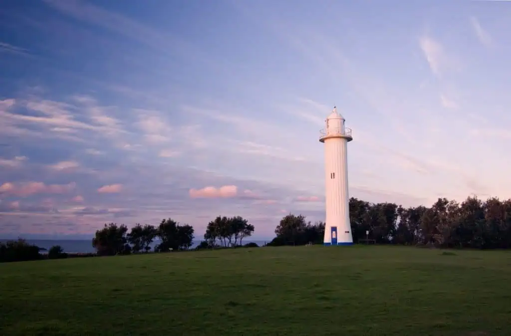Yamba Lighthouse standing tall on a grassy headland under a pastel sunset sky, a peaceful lookout along the scenic road trip between Sydney and Byron Bay.
