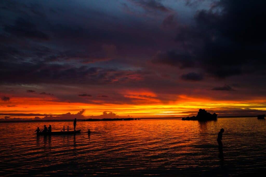 Silhouetted figures in the water at sunset on Lord Howe Island, with the sky glowing in deep orange and red hues. This image showcases Lord Howe Island as one of the top destinations for sunsets in Australia.