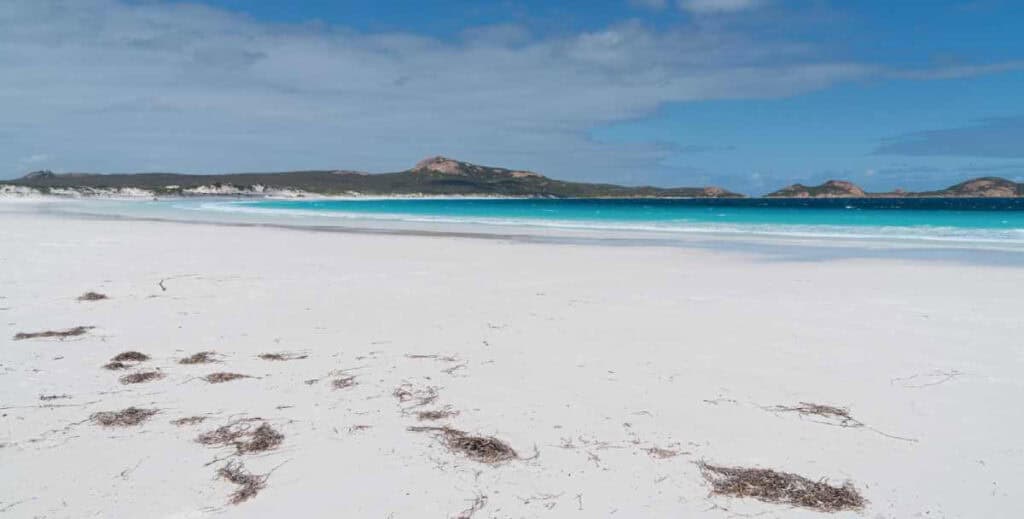 The unspoiled beauty of Lucky Bay, with its brilliant white sand and crystal-clear waters, stands out as one of the stunning coastal gems in Western Australia's beachescape, backed by the distant peaks of the Recherche Archipelago.