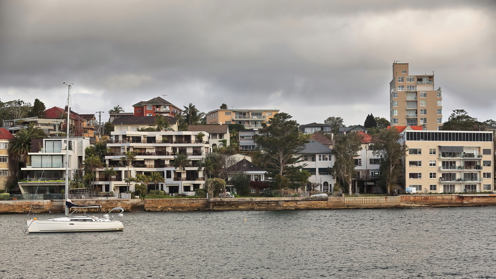 North Head peninsula harborside lined with waterfront residential buildings facing Manly Cove and moored sailboat as seen from the Manly to Sydney ferry starting its trip. 