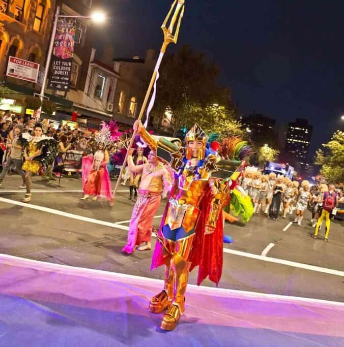 Person dressed in a golden warrior costume leading a colourful street parade at night during Sydney Mardi Gras, one of the most epic festivals in Australia celebrating pride, diversity, and self-expression.