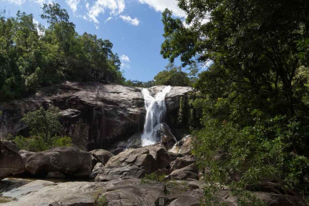 Murray Falls in Queensland, where water cascades over large rocky surfaces surrounded by dense, tropical greenery. This stunning waterfall is a prime example of the top waterfalls in Queensland and offers a serene natural escape for visitors.