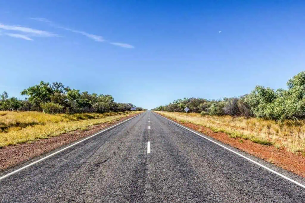 A long, straight road through the Nullarbor Plain under a clear blue sky, symbolising the vast distance and journey from Perth to Adelaide.