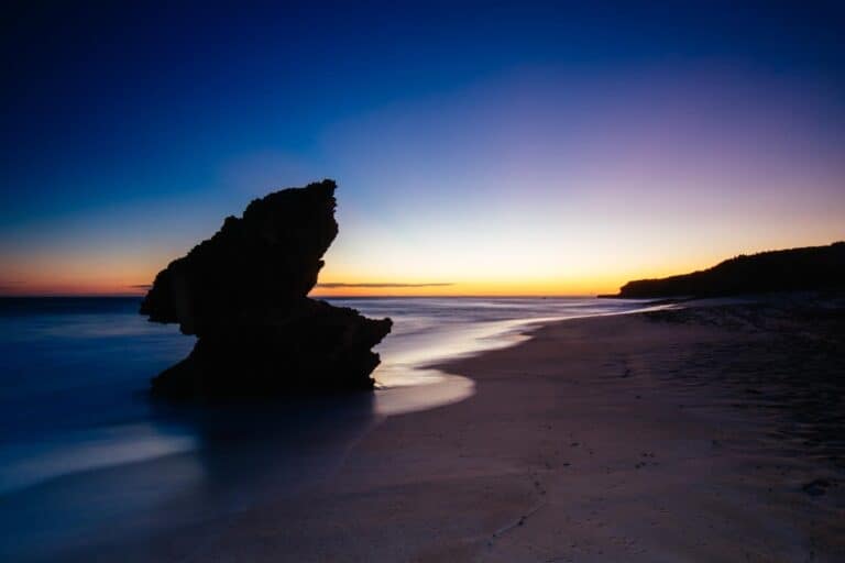 Number 16 Beach in Rye, Australia, with a striking rock formation silhouetted against the sunset. While visually captivating, this spot is often considered one of the least safe beaches in Australia for swimming, due to powerful waves and dangerous rips that pose risks to visitors.