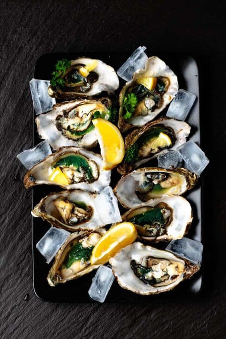 Freshly shucked oysters served on a black platter with ice and lemon wedges, showcasing the seafood offerings at Poyers, one of the best restaurants in Port Stephens for quality seafood. This vibrant dish highlights the restaurant's commitment to fresh, local ingredients, making it a popular dining choice in the region.