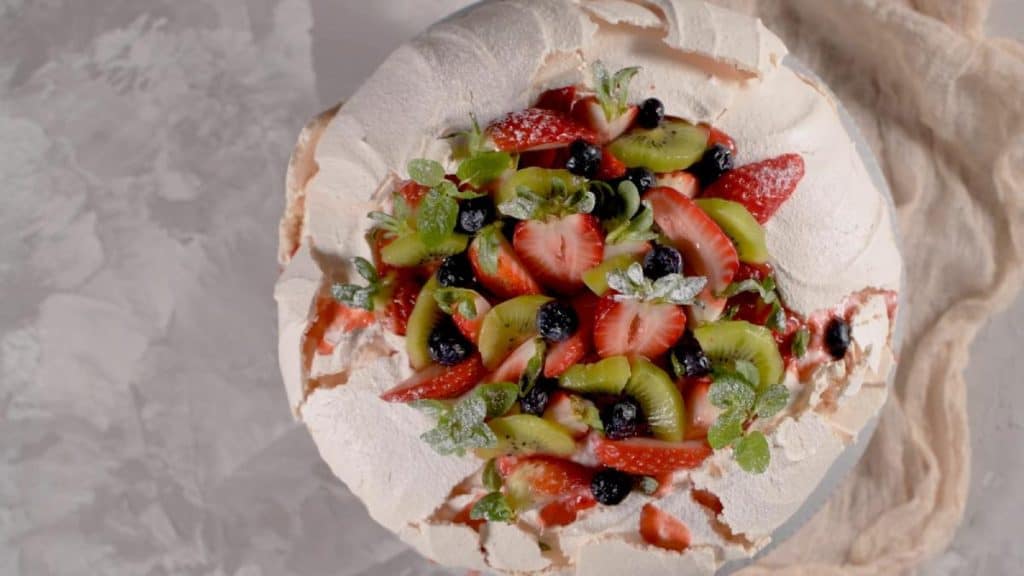 A festive pavlova topped with fresh strawberries, kiwi, and blueberries, a classic Christmas dessert treat perfect for summer celebrations