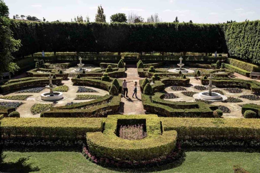 A couple walking through a manicured garden with fountains and sculpted hedges in Pokolbin, Hunter Valley. This peaceful setting reflects the lifestyle benefits mentioned when exploring what it's like to live in Hunter Valley, including the pros and cons of settling in a scenic wine region.