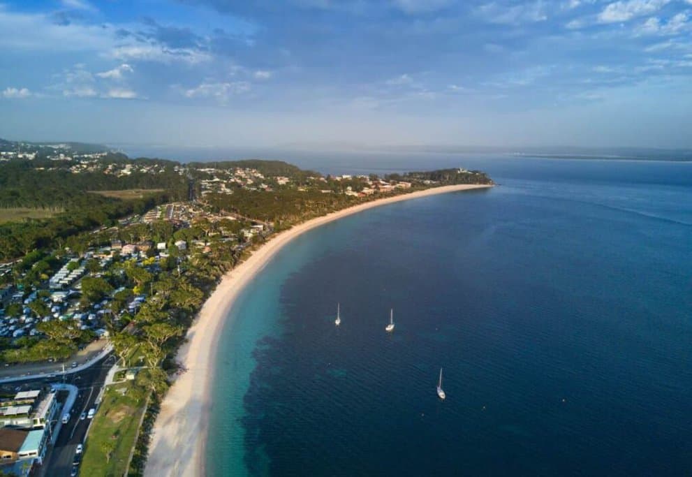 Aerial view of the coastline and beach at Port Stephens, featuring pristine waters and lush surroundings, often highlighted in travel deals in Australia.