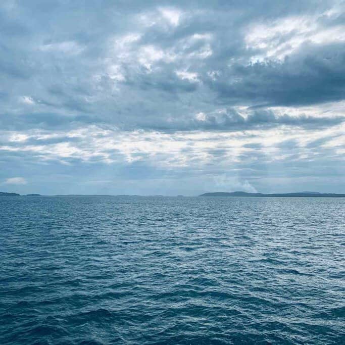 A serene view of the blue ocean under a cloudy sky in Port Stephens, illustrating the tranquil conditions often ideal for spotting dolphins. This image complements the post discussing the best times for dolphin watching in Port Stephens.