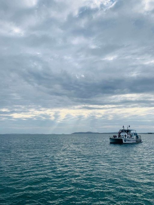 A dolphin-watching tour boat floating on the calm waters of Port Stephens under a cloudy sky, showcasing a popular activity during the best times for dolphin watching in this region.