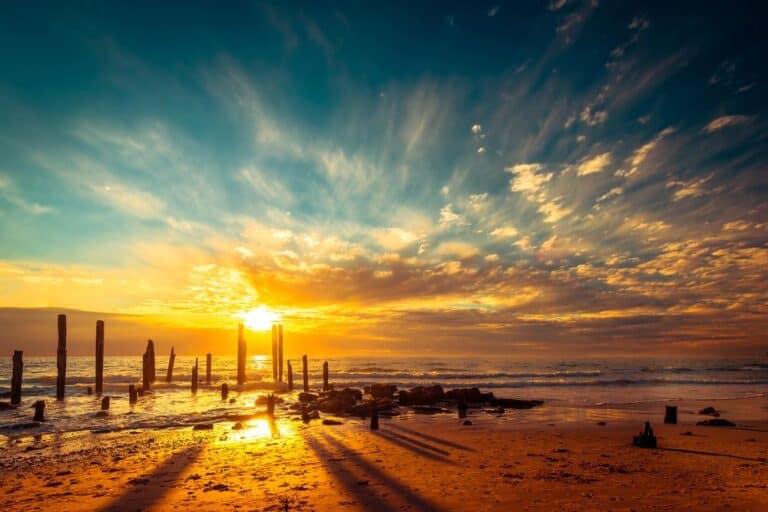 Golden sunset over the remains of the jetty at Port Willunga Beach, South Australia, with vibrant colours in the sky reflecting on the sand and ocean. This image showcases Port Willunga as one of the breathtaking sunsets across Australia.