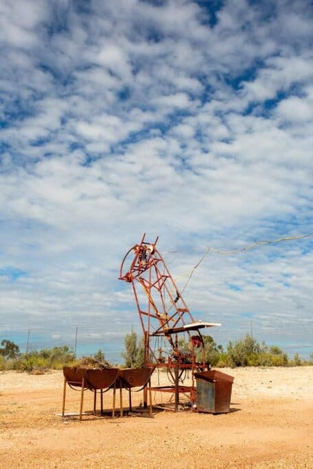 A rustic opal mining contraption in Lightning Ridge, surrounded by red dirt and scrub under a cloudy sky – highlighting the region’s unique character and its connection to black opal mining, one of the lesser-known yet fascinating facts about New South Wales.