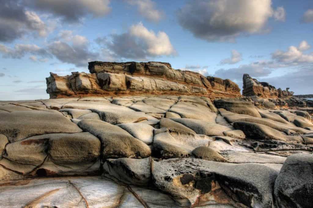 Weathered rock formations along the Yamba coastline under a cloudy sky, showcasing the raw natural beauty found on a road trip from Sydney to Byron Bay.