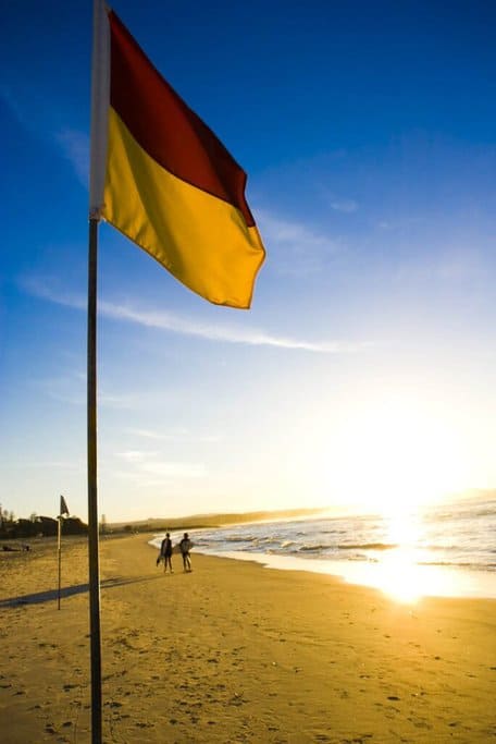 A red and yellow flag marking a safe swimming area on an Australian beach at sunset, symbolizing the importance of following safety guidelines to 'travel safe in Australia' and enjoy the country's stunning coastlines securely.