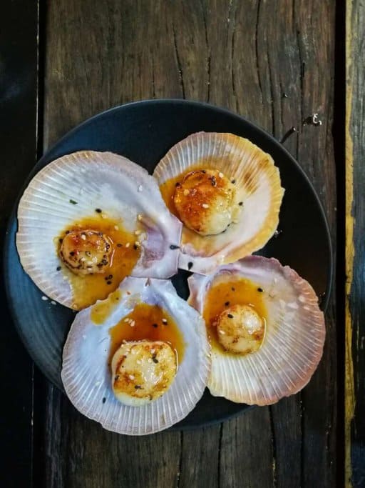 Grilled scallops served in their shells with a rich glaze and sesame seeds, a signature dish at Rick Stein at Bannisters, one of the best restaurants in Port Stephens. The beautifully presented scallops highlight the restaurant's focus on fresh seafood and innovative flavours, offering diners a memorable culinary experience in Port Stephens.