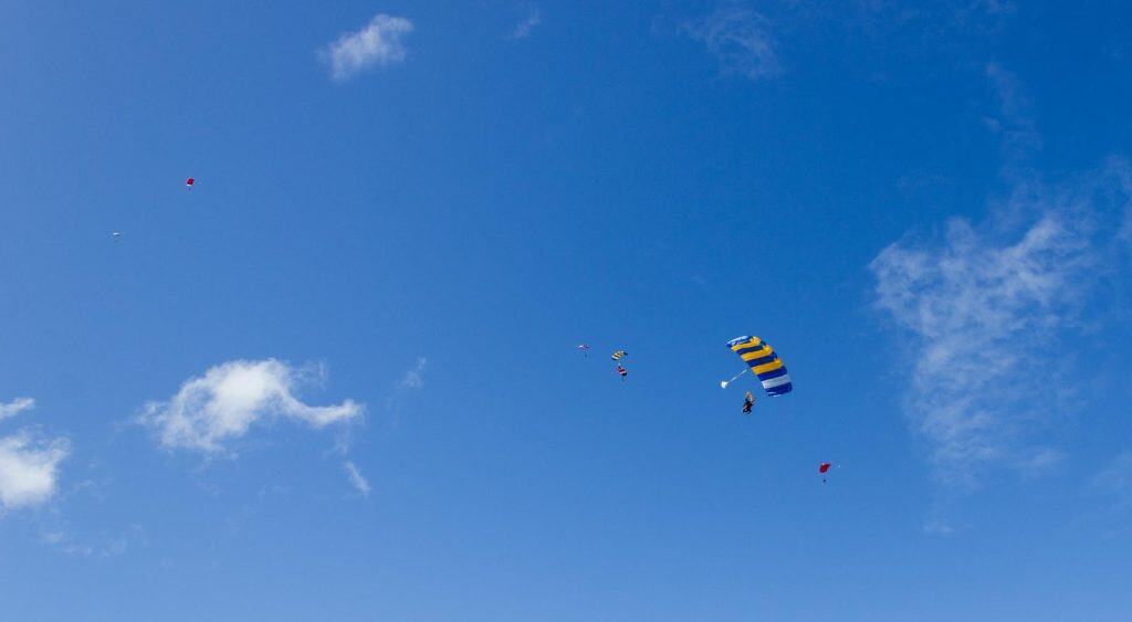 Group of skydivers floating under colourful parachutes against a clear blue sky during a tandem jump, one of the most adventurous activities to try in Byron Bay.