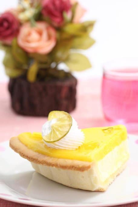 A slice of lemon cheesecake topped with whipped cream and lime, a refreshing and vibrant dessert often enjoyed during Australia's Christmas celebrations.