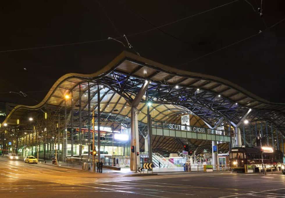 Night view of Southern Cross Station in Melbourne, showcasing the modern architecture and a tram passing by. This station is a key hub for connecting major routes, including the Adelaide to Sydney train journey.