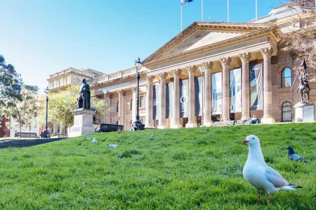 Exterior view of the State Library of Victoria in Melbourne with a statue and seagulls in the foreground, providing a scenic location near some of the best Christmas lunch spots in Melbourne, ideal for holiday dining and sightseeing.