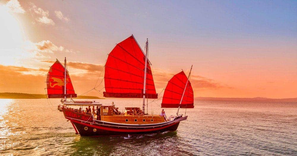 Traditional shaolin boat with vibrant red sails cruising at sunset, offering a picturesque sailing experience, a top activity for those looking to explore things to do in Port Douglas.