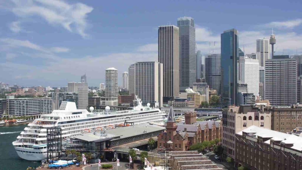 A view of Sydney Harbour with a cruise ship docked, set against the backdrop of the city's skyscrapers. This image relates to the topic 'how to stay safe in Australia,' highlighting the importance of staying informed and prepared when exploring Australia's urban and coastal environments.