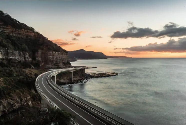 A stunning coastal view of the Sea Cliff Bridge at sunset, part of the scenic route on the Sydney to Grand Pacific Drive, highlighting the picturesque landscapes travelers can enjoy on this journey.