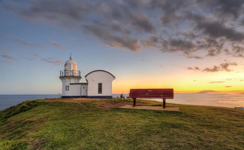 Tacking Point Lighthouse in Port Macquarie glowing at sunset with a bench overlooking the sea, a serene photo stop on the drive between Sydney and Byron Bay.