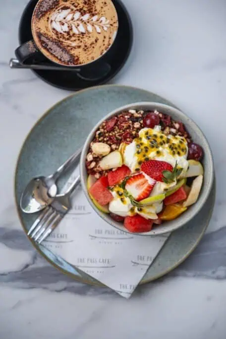 Colourful fruit and granola bowl with yoghurt and a cappuccino served at The Pass Café, one of the top foodie stops to include on your Byron Bay itinerary.