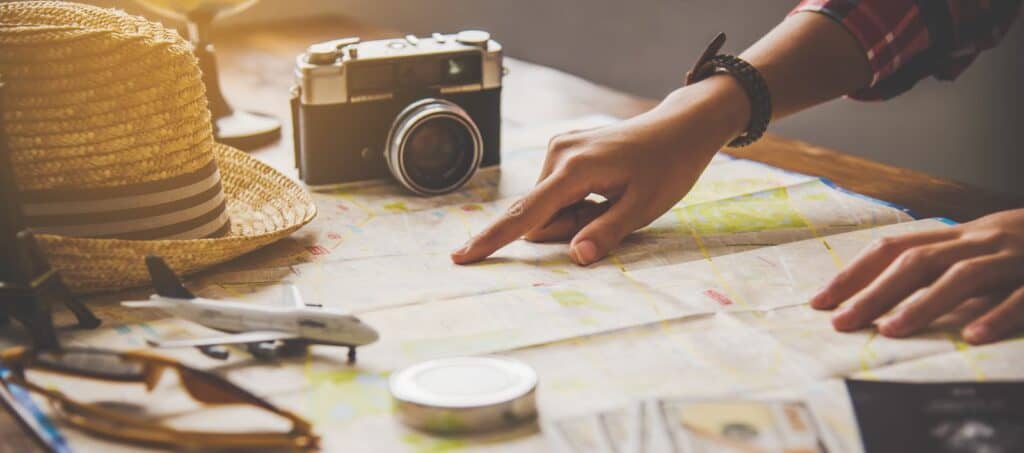A person planning a trip by pointing at a map, surrounded by travel essentials like a camera and hat, symbolizing the preparation needed to ensure safety while travelling. This image relates to the blog's focus on answering the question 'is it safe in Australia' and the importance of careful planning for a secure and enjoyable visit.