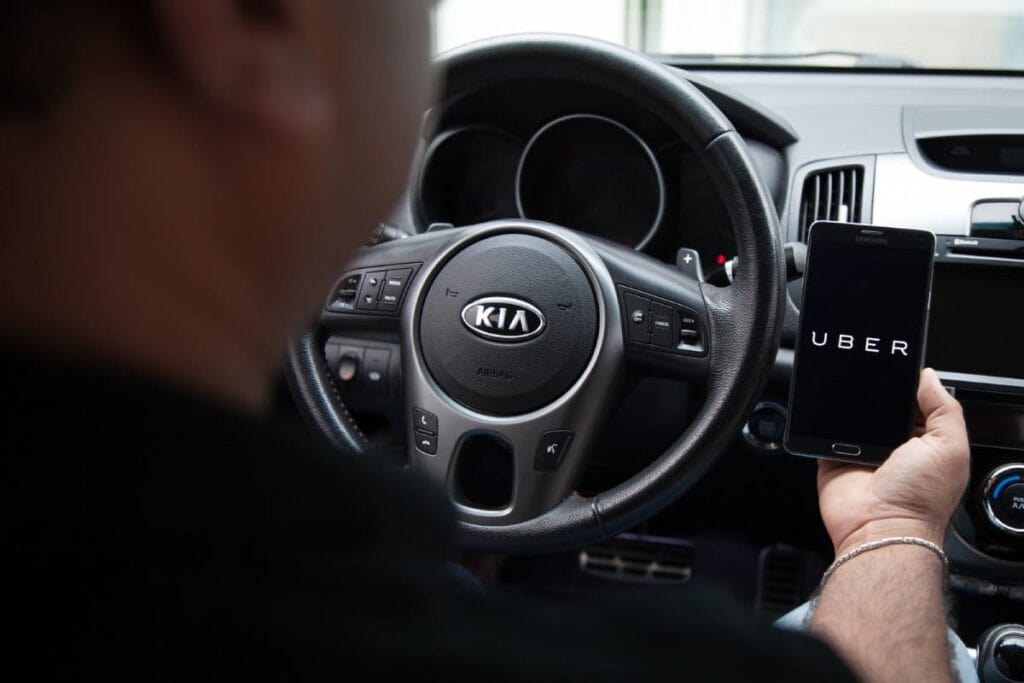 Driver in a Kia car holding a smartphone with Uber app, illustrating Uber usage in Melbourne for convenient city transportation.