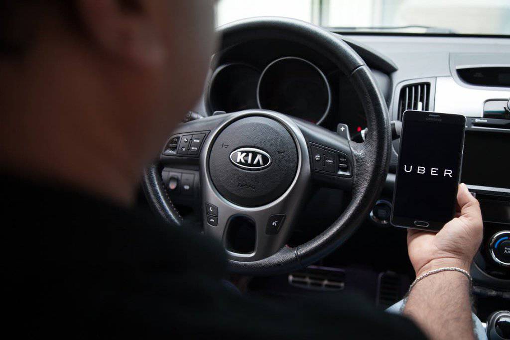 Driver in a Kia car holding a smartphone with Uber app, illustrating Uber usage in Melbourne for convenient city transportation.