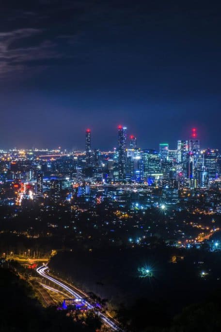A dazzling nighttime view of Brisbane's city skyline illuminated with vibrant lights, seen from Mount Coot-tha, a highlight of Queensland's best scenic drives.