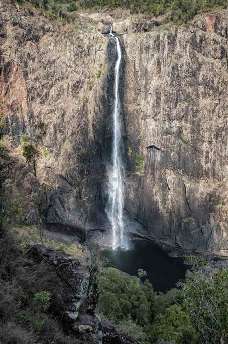 Wallaman Falls, a stunning single-drop waterfall cascading from a high cliff into a deep pool surrounded by lush greenery. This magnificent waterfall is often regarded as one of the must-visit natural wonders in Queensland, offering breathtaking views and a serene atmosphere for visitors.