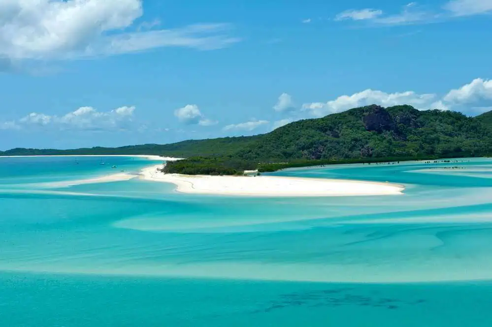 The striking beauty of Whitehaven Beach with its swirling white sands and varying shades of blue waters, surrounded by lush greenery, capturing the breathtaking tranquility of beaches in Australia.
