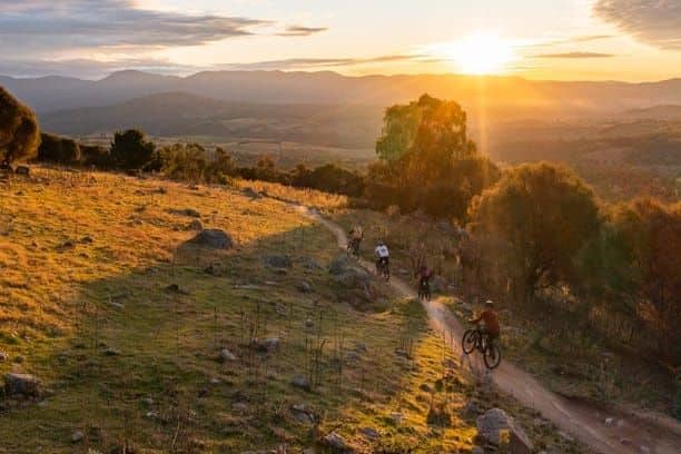 Four cyclists enjoying a scenic bike path in the hills at sunset, highlighting the outdoor lifestyle as one of the pros of living in Canberra.