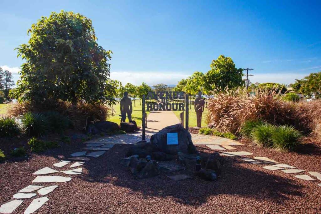 Yungaburra Avenue of Honour featuring a pathway with sculptures and trees under a clear blue sky, commemorating fallen soldiers. This memorial is one of the meaningful cultural sites to visit in the Atherton Tablelands.